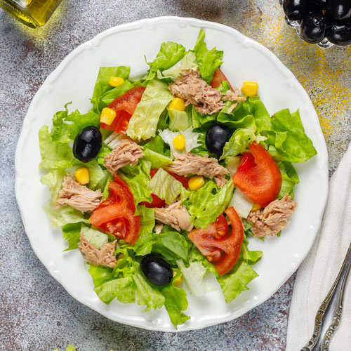 Tuna salad with lettuce olives corn tomatoes top view